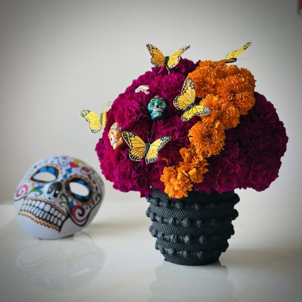Marigold arrangement in a black vase with butterfly picks and a decorative skull beside it
