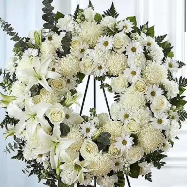 White floral wreath on a black easel with lilies and roses
