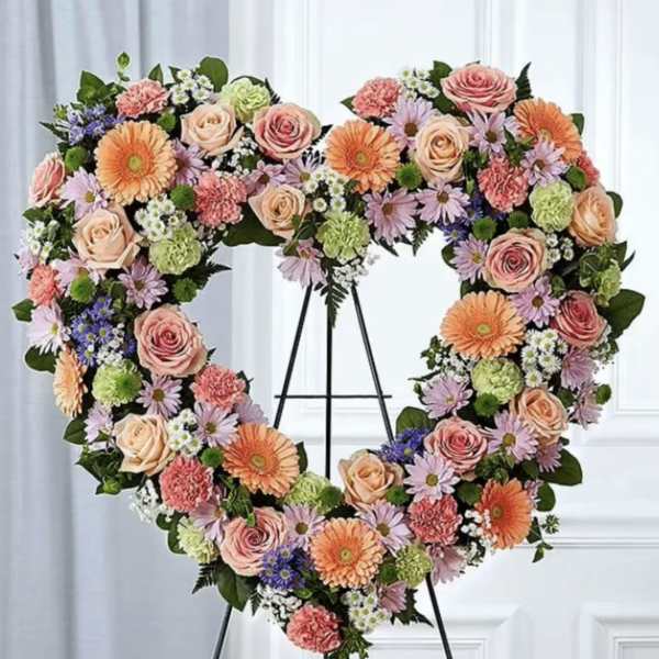 Heart-shaped floral wreath on a black stand with pink, peach, and purple flowers