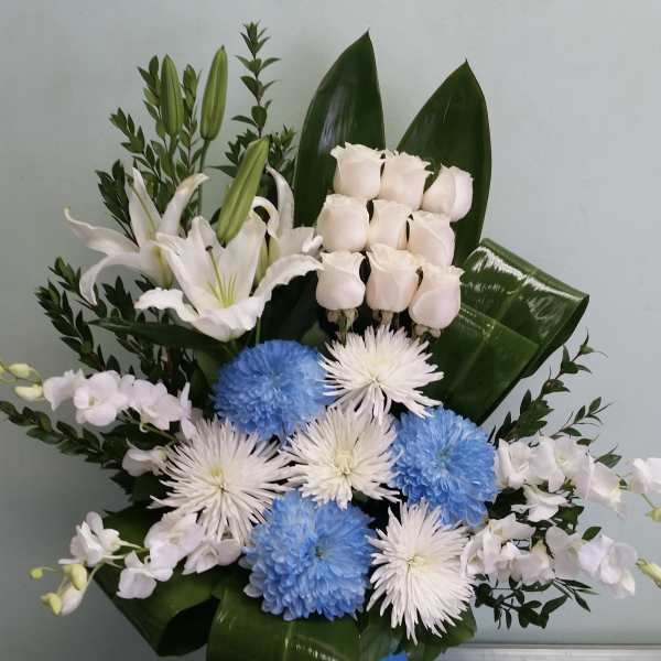 White lilies, pale roses, and blue and white chrysanthemums in a box arrangement