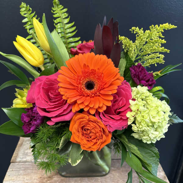 Bright mixed bouquet with orange gerbera, pink roses, and yellow tulips in a glass vase