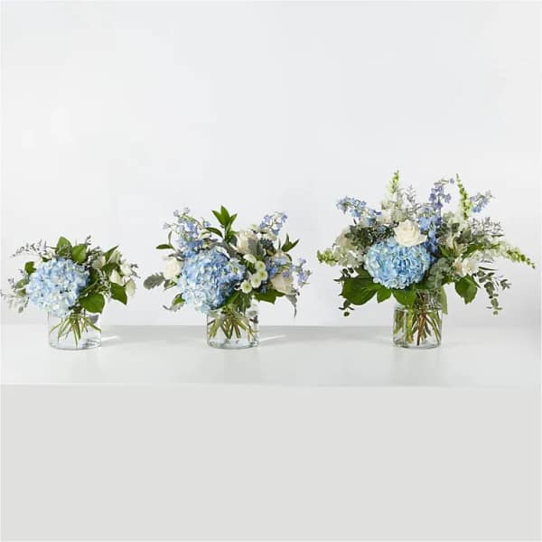 Three blue and white floral arrangements in clear glass vases