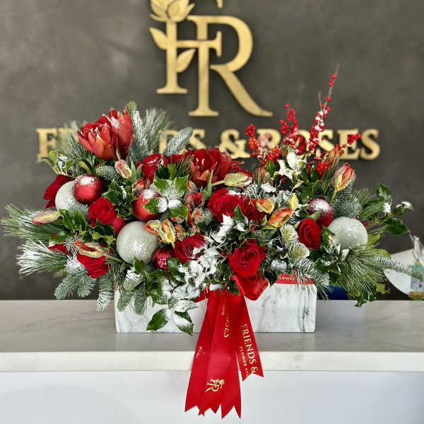 Red roses and holiday flowers in a white rectangular vase with ornaments