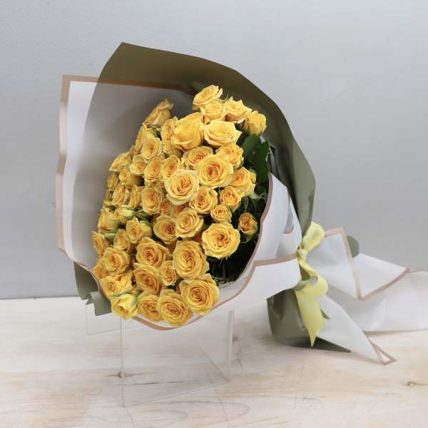 Large bouquet of clustered yellow roses wrapped in white and green paper with a bow