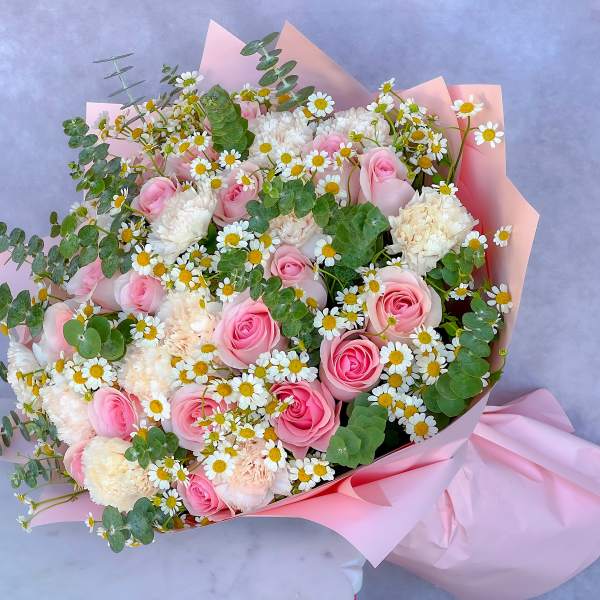 Bouquet of pink roses, white carnations, and daisies wrapped in pink paper