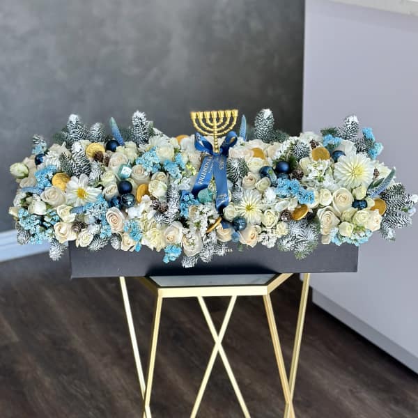 White rose arrangement with blue accents and a gold menorah topper in a black box