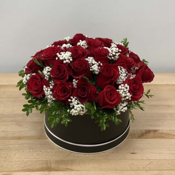 Red roses arranged in a round black box with white filler flowers