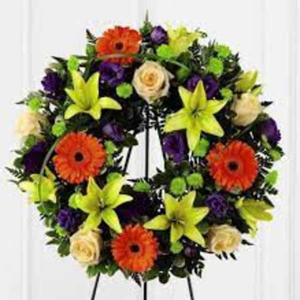Circular floral wreath with orange gerberas, yellow lilies, cream roses, and purple blooms