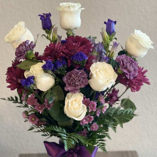 Bouquet of white roses, purple blooms, and a purple ribbon in a glass vase
