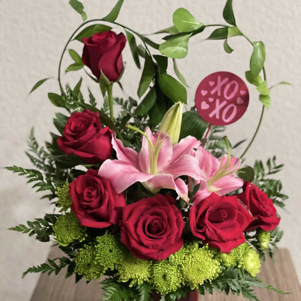 Red roses and pink lilies arranged in a red vase with a heart sign