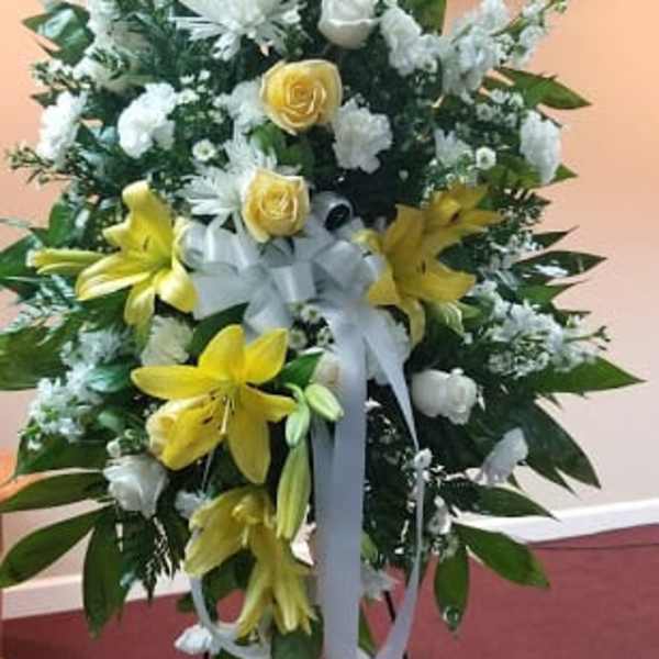 Standing floral spray with yellow lilies, white roses, and a white ribbon