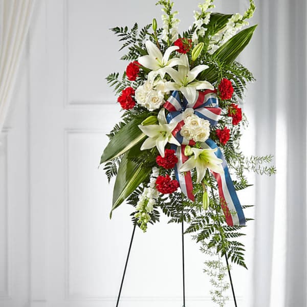 Standing floral spray with white lilies, red carnations, and ribbon on an easel