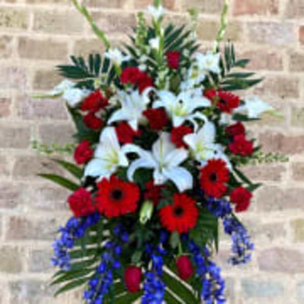 Standing floral spray with white lilies, red gerberas, and blue accents