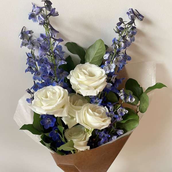 Bouquet of white roses and blue delphinium wrapped in brown paper