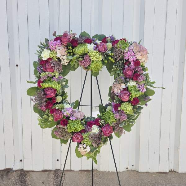 Heart-shaped standing wreath with pink roses, hydrangeas, and green mums on a metal easel