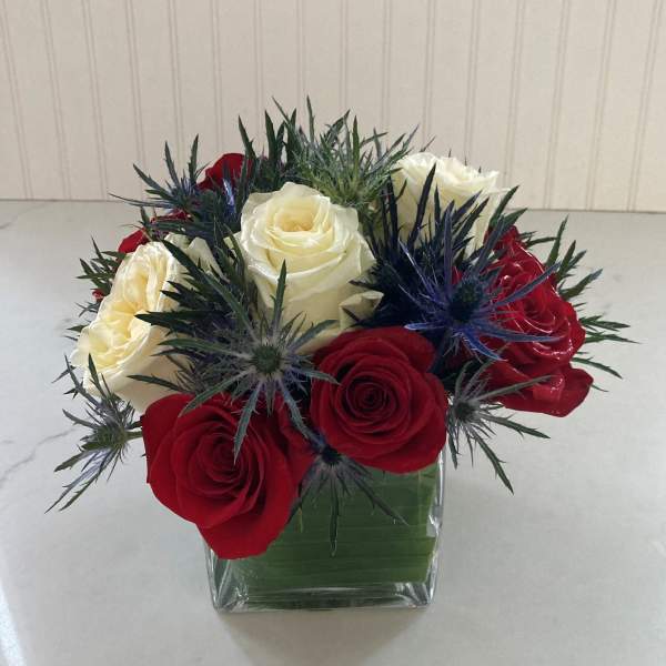 Red and white roses in a square glass vase with spiky blue thistle