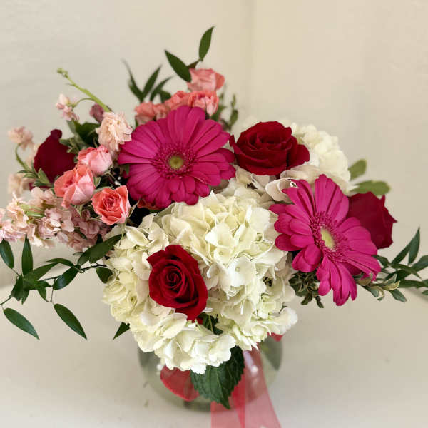 Bouquet of red roses, pink gerberas, and white hydrangeas in a glass vase