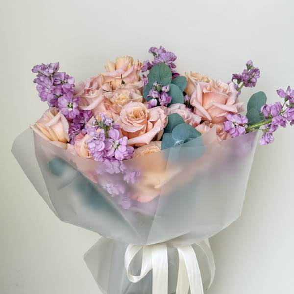 Bouquet of blush roses and purple flowers in a glass vase