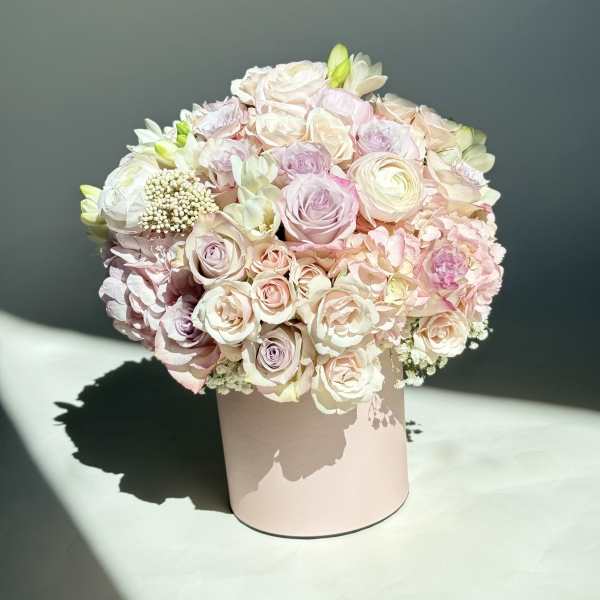 Round pastel bouquet of roses and ranunculus in a blush box
