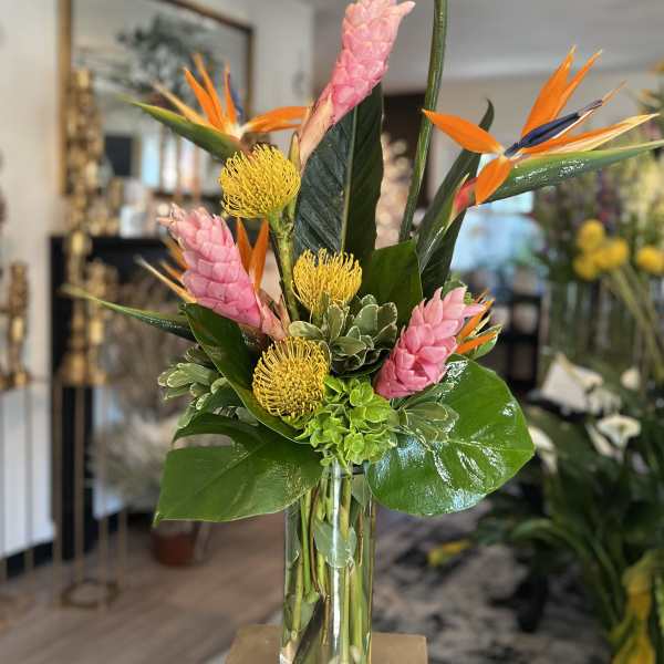 Tall tropical bouquet in a clear glass vase with pink and orange blooms