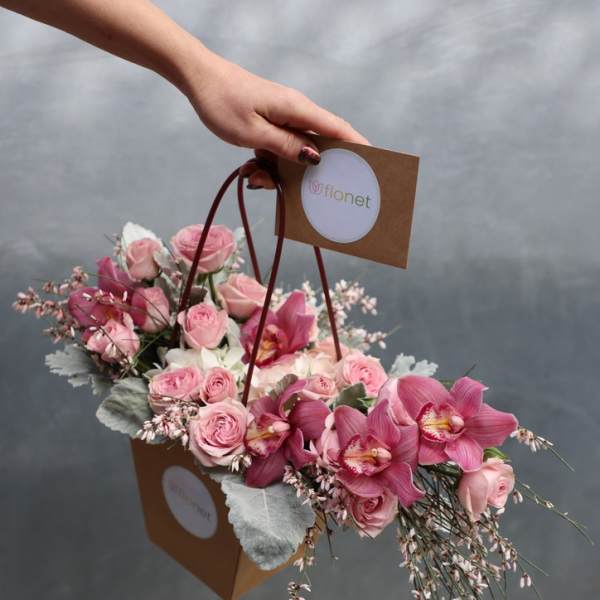Pink roses and orchids in a brown handled gift bag