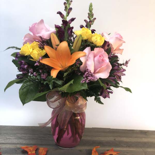 Mixed bouquet of pink roses, orange lilies, and yellow blooms in a vase