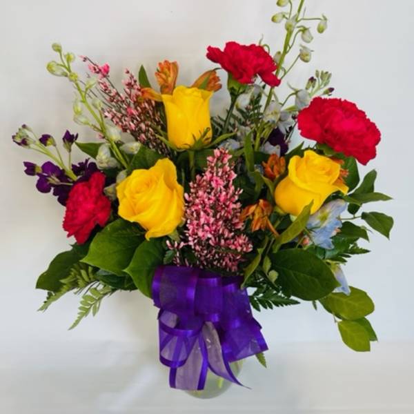 Mixed bouquet of yellow and red roses with purple accents in a glass vase