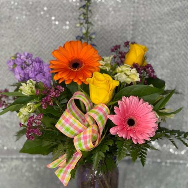 Colorful bouquet of gerbera daisies and roses in a purple vase with a plaid ribbon
