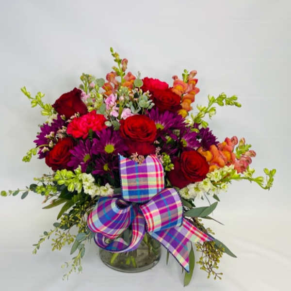 Bouquet of red roses, purple daisies, and orange snapdragons in a glass vase with a plaid bow
