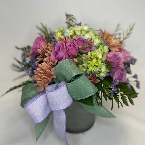Bouquet of pink, purple, and yellow flowers with a lavender ribbon in a vase