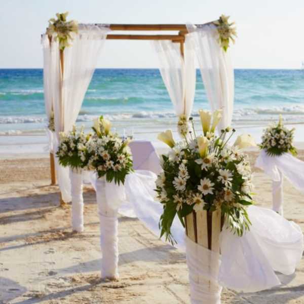 Beach wedding arch with white drapes and floral arrangements