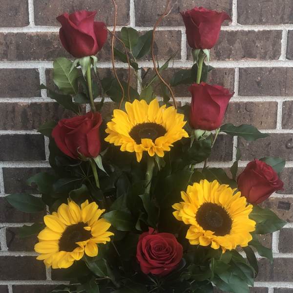 Red roses and yellow sunflowers in a vase with a pink ribbon