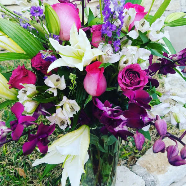 Bouquet of pink roses, white lilies, and purple orchids in a glass vase