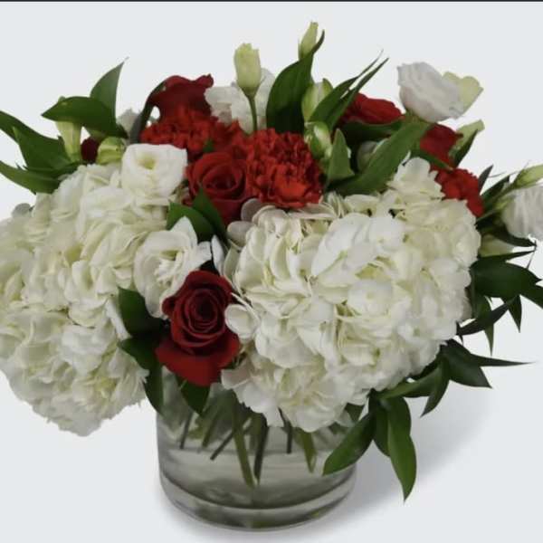 White hydrangeas and red roses arranged in a clear glass vase
