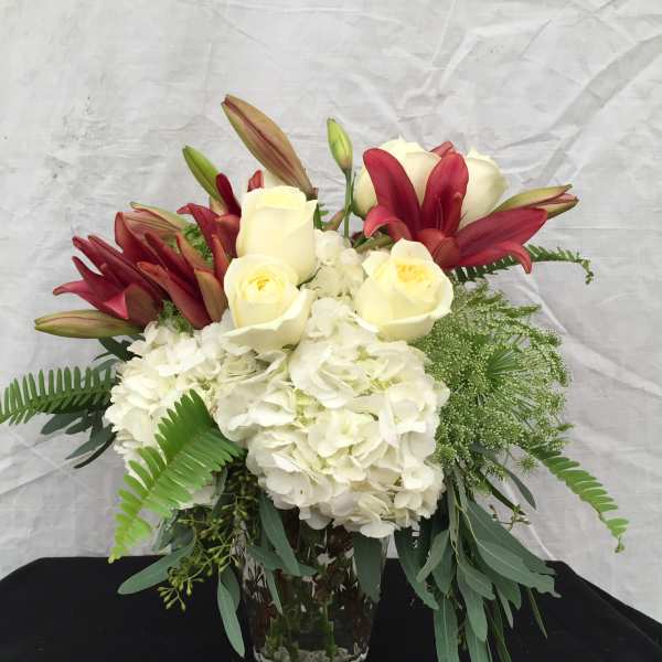 White hydrangeas with ivory roses and red lilies in a clear glass vase