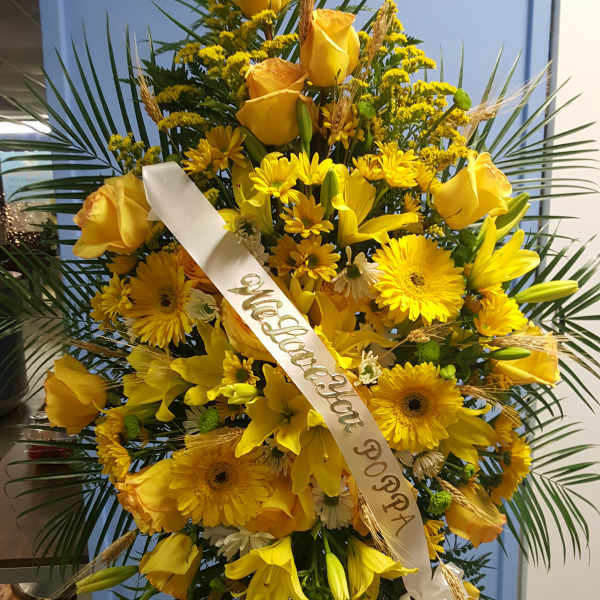 Tall yellow floral standing spray with a white ribbon on an easel