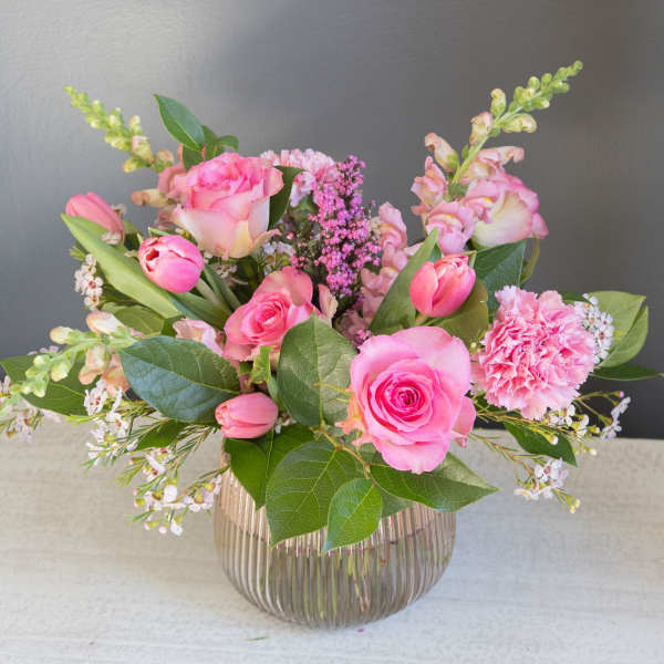 Pink roses and tulips arranged in a ribbed glass vase