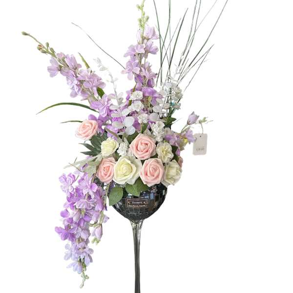 Tall floral arrangement in a wine glass-shaped vase with pink and lavender blooms