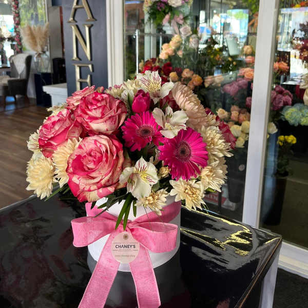 Pink and cream mixed flower arrangement in a white hat box with a pink ribbon