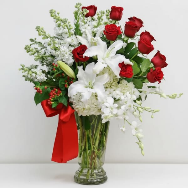 Red roses and white lilies in a clear glass vase with a red ribbon