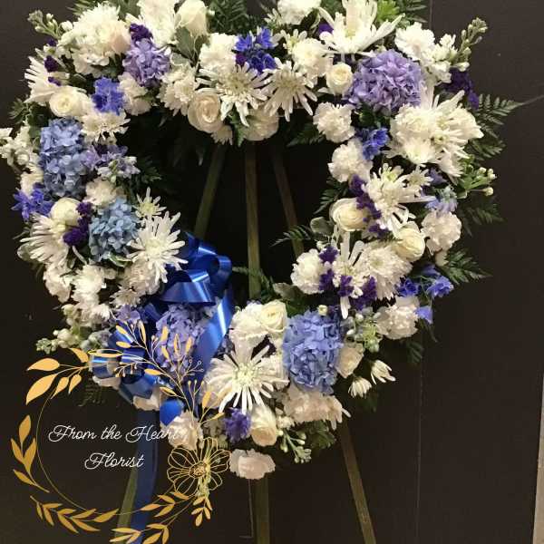 Heart-shaped white and blue floral wreath on an easel with a blue ribbon
