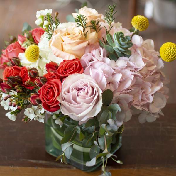 Mixed bouquet of roses, hydrangeas, and succulents in a green glass vase