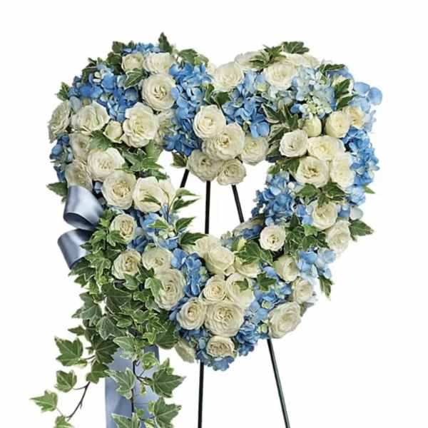 Heart-shaped floral wreath with white and blue flowers on a stand