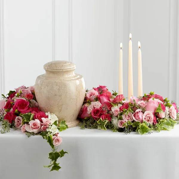 Pink rose floral centerpiece with a beige urn and three taper candles
