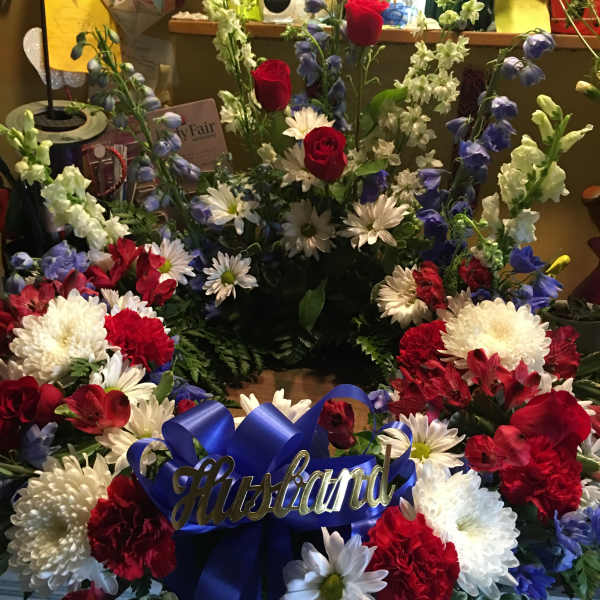 Floral arrangement with red roses, white daisies, and blue flowers with a blue ribbon