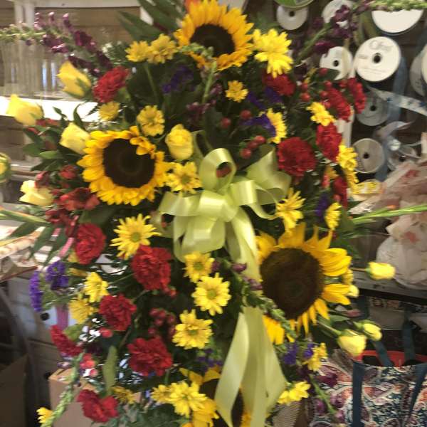 Large standing floral spray with sunflowers, red carnations, and yellow roses