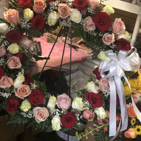 Large circular wreath of red, pink, and white roses with a white ribbon bow