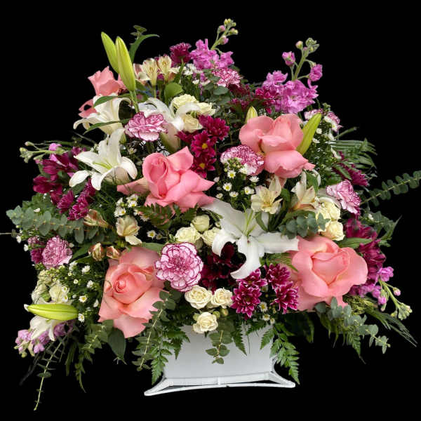 Large mixed floral arrangement with pink roses and white lilies in a white container