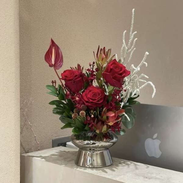 Red rose arrangement in a silver vase with white decorative branches