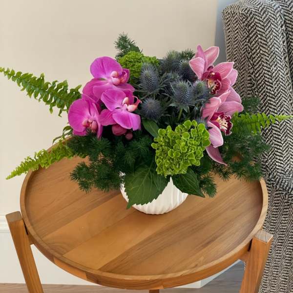 Pink orchids and blue thistle in a white vase